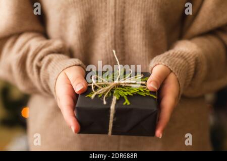 Womans Hände halten schöne Geschenk in schwarzem Papier eingewickelt und mit grünen Zweig verziert, Nahaufnahme Stockfoto