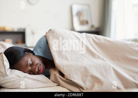 Minimalportrait einer jungen afroamerikanischen Frau, die glücklich auf Weiß schläft Baumwollbettwäsche in gemütlicher Wohneinrichtung Stockfoto