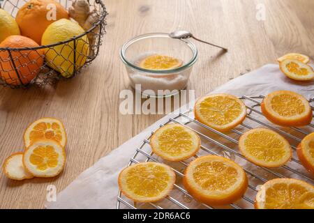 Kandierte Orangen Konzept: Eine Schüssel mit Zucker mit einer Orangenscheibe und einem Löffel, und Orangenscheiben auf einem Holztisch. Stockfoto