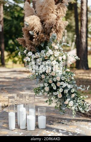 Hochzeitszeremonie. Bogen, geschmückt mit Blumen und Kerzen auf dem Rasen, Bäume Hintergrund, im Sommer. Stockfoto