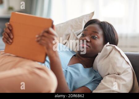 Porträt einer jungen afroamerikanischen Frau, die morgens auf dem Bett liegt und mit digitalem Tablet, Kopierraum benutzt Stockfoto