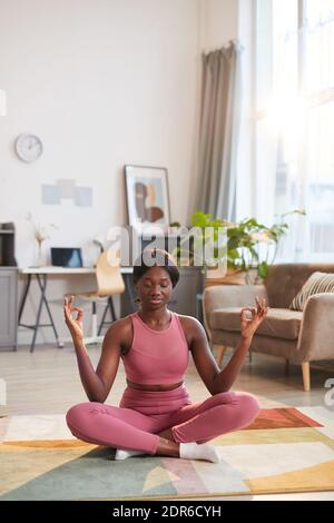Vertikales Porträt einer jungen afroamerikanischen Frau, die während der Sportkleidung rosa trägt Yoga-Training zu Hause Stockfoto