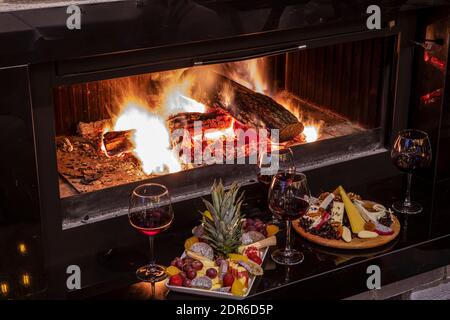 Käse- und Obstteller auf dem Tisch am Kamin. Ein üppiges Fest mit frischem Obst und Gemüse, rustikalem Brot, Käse und Wein im Glas auf einem Stockfoto