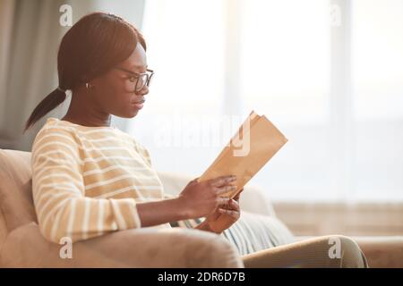 Seitenansicht Porträt der jungen afroamerikanischen Frau Lesung in gemütlichen Wohnräumen, Kopierer Raum Stockfoto