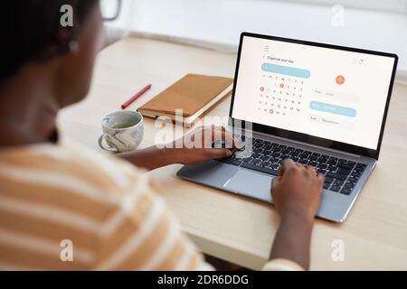 Porträt der jungen afroamerikanischen Frau mit Zeitmanagement-Website während Laptop am Schreibtisch Stockfoto