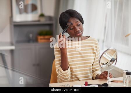 Porträt einer jungen afroamerikanischen Frau, die mit großem Pinsel unterwegs ist Make-up durch Spiegel Stockfoto