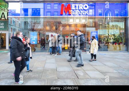 Metro Bank Storefront, Fassade, Market Street, Manchester City Centre. Drei Personen nutzen einen geldautomaten oder Geldautomaten, während Fußgänger vorbei gehen. Dezember 2020 Stockfoto