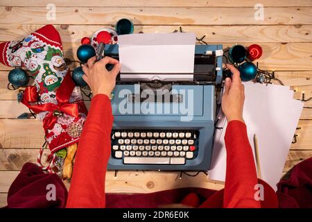 Weihnachtliche Atmosphäre mit einer Vintage-Schreibmaschine, Strümpfen voller Süßigkeiten, einer roten Decke und einem Stapel leerer Blätter. Stockfoto