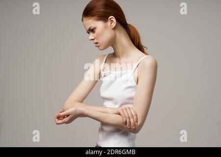 Rothaarige Frau in einem weißen T-Shirt auf beigem Hintergrund Gestikulieren mit ihren Händen Schmerzen im Ellbogen Stockfoto