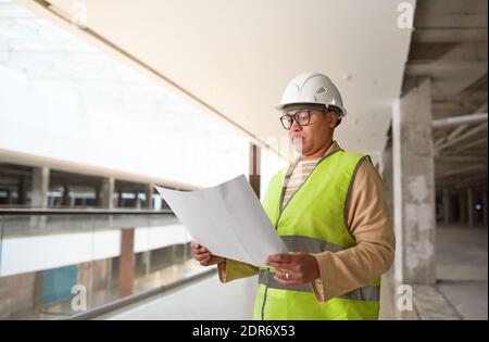 Waist-up-Porträt von Mixed-Race-Ingenieurin hält Blaupausen während der Arbeit auf der Baustelle, kopieren Raum Stockfoto