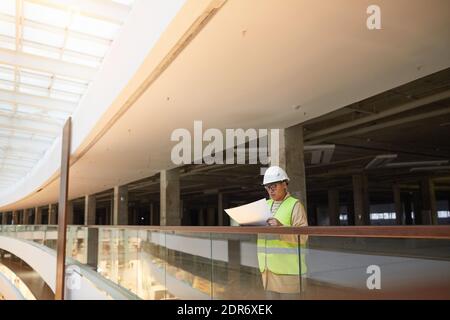 Weitwinkel-Porträt von Mixed-Rennen weibliche Ingenieurin hält Blaupausen während der Arbeit auf der Baustelle, kopieren Raum Stockfoto