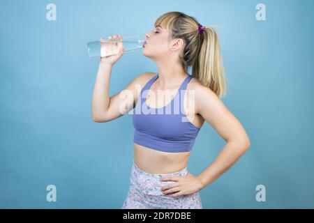 Junge schöne Frau trägt Sportkleidung mit einer Flasche Wasser Über isoliertem blauem Hintergrund Trinkwasser Stockfoto