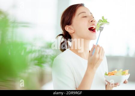 Junge glückliche Frau essen gesunden Salat zu Hause Stockfoto