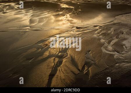 Die abgehende Flut spiegelt die untergehende Sonne auf dem Strandsand am Parker River National Wildlife Refuge in Newbury, MA USA Stockfoto