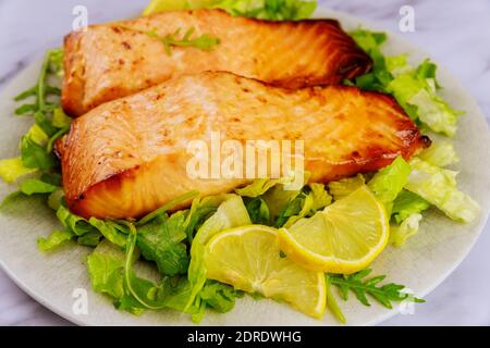 Nahaufnahme des gekochten Lachsfilets auf dem Teller mit Zitrone und Salat. Stockfoto