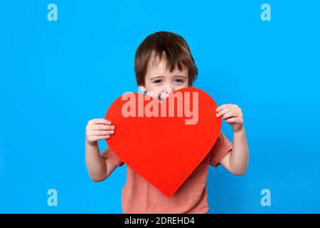 Portrait von stilvollen kleinen Jungen mit großen roten Herzen blau Hintergrund Stockfoto