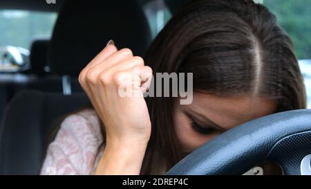 Traurige und müde Frau, die ihren Kopf auf das Lenkrad lehnte und weinte, während sie im Auto saß. Stockfoto