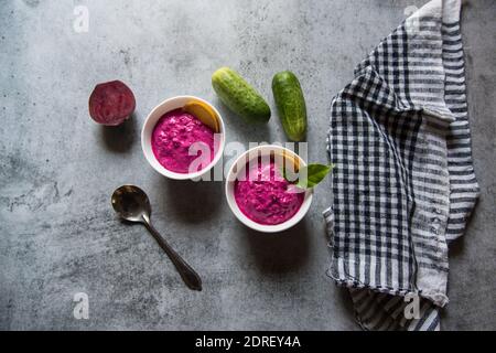 Rote Beete Dip serviert in zwei kleinen Schüsseln zusammen mit Gemüsewürzen auf einem Hintergrund. Stockfoto