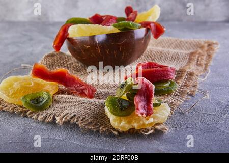 Getrocknete Früchte: Gelb kandierte Ananasringe, rote Papaya und grün in einem Holzteller auf Sackleinen Stockfoto