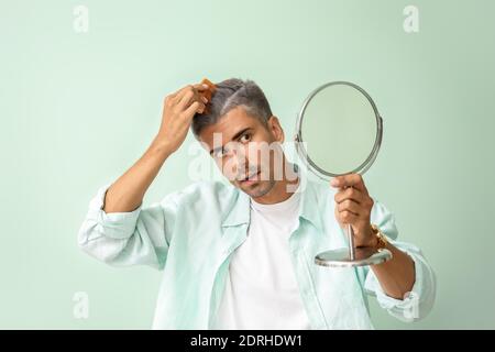 Gestresster Mann mit grauem Haar in Spiegel auf Farbe suchen Hintergrund Stockfoto