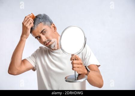 Mann mit grauem Haar, der im Spiegel auf hellem Hintergrund schaut Stockfoto