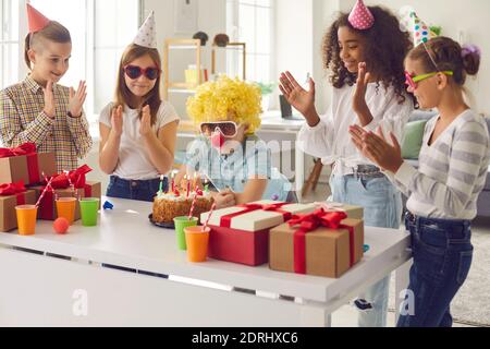 Junge gekleidet als Clown machen seinen Geburtstagswunsch vor dem Blasen Kerzen auf Kuchen auf Party mit Freunden Stockfoto