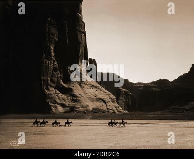 Vintage-Foto von 1904 von Edward S Curtis von sieben Reitern auf dem Pferd und Hund Trekking vor dem Hintergrund der Canyon Klippen. Canyon De Chelly. Stockfoto