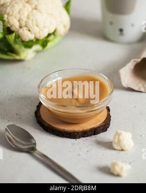 Baby Püree in einem Blumenkohlteller mit einem Löffel, neben frischem Blumenkohl. Layout Babynahrung Konzept, erste Fütterung. Stockfoto