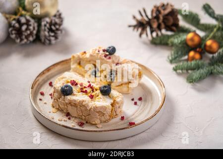 Zwei Stück Baiser-Rollkuchen mit Sahne, Beeren und Mandel auf dem Teller, selektiver Fokus, im Hintergrund Christbaumzweige mit Zapfen und Spielzeug Stockfoto