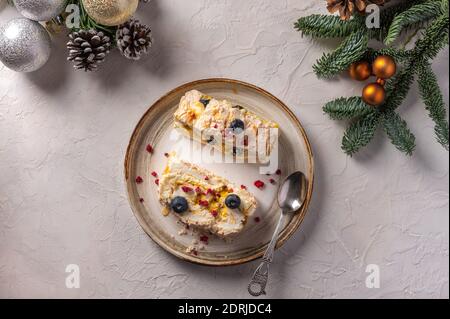 Hausgemachte zwei Stücke von Meringue Roll Kuchen mit Sahne, Beeren und Mandel auf dem Teller, selektive Fokus, im Hintergrund Weihnachtsbaum Äste mit Zapfen und Spielzeug, Draufsicht Stockfoto