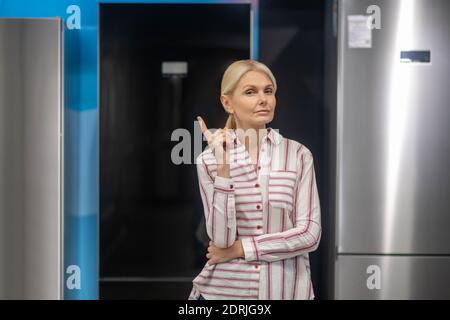 Blonde Frau im gestreiften Hemd Auswahl Kühlschrank in einem Showroom Stockfoto