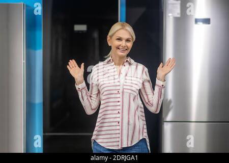 Blonde Frau im gestreiften Hemd Auswahl Kühlschrank in einem Showroom Stockfoto