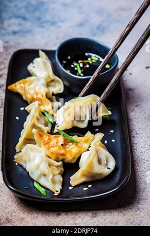 Gebratene Gyoza-Knödel mit Sauce und grünen Zwiebeln auf schwarzem Teller, dunkler Hintergrund. Konzept der japanischen Küche. Stockfoto