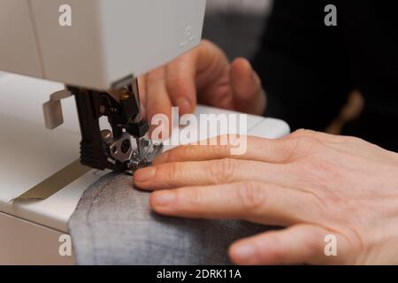 Detail der Nähmaschine mit menschlichen Händen Nähen zusammen zwei Stoffstücke für die Herstellung von Schutzmasken zu Hause Während des Lockdown von Covid crisi Stockfoto