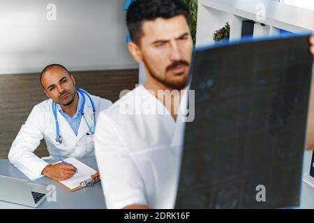 Zwei männliche Ärzte untersuchen MRT-Hirnscans eines Patienten Im Schrank Stockfoto