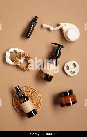 Kosmetikflaschen aus braunem Glas und weibliche Accessoires auf braunem Schreibtisch. Flach liegend, Draufsicht. Bio-Beauty-Produkte Verpackung Design, Branding Stockfoto