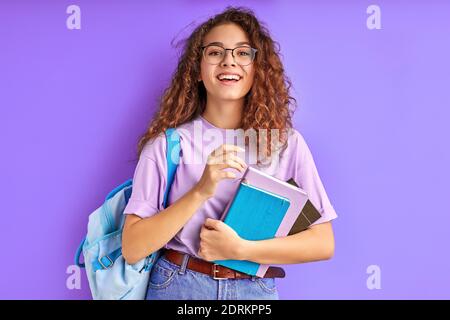 Junge schöne Schulmädchen mit lockigen Haaren scharf auf das Studium, Vorbereitung für die Schule oder Hochschule, isoliert lila Hintergrund Stockfoto