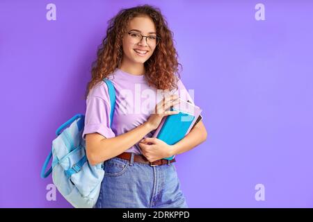 Junge schöne Schulmädchen mit lockigen Haaren scharf auf das Studium, Vorbereitung für die Schule oder Hochschule, isoliert lila Hintergrund Stockfoto