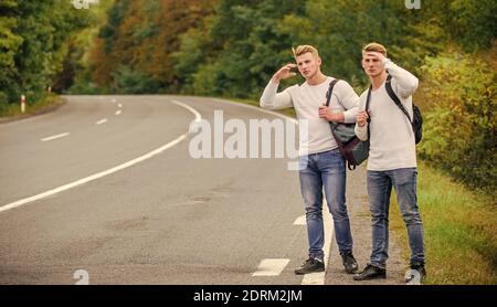 Budget Reisende. Männer Rucksäcke zu Fuß zusammen auf der Straße. Zwillinge zu Fuß entlang der Straße. Abenteuer und Entdeckung. Mann mit Rucksack Anhalter auf der Straße. Sommerurlaub. Automatischer Stopp für Reisende. Stockfoto