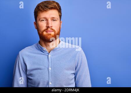 Rotschopf Mann in formellen Hemd Blick auf Kamera, angenehm bärtigen Kerl isoliert über blauen Hintergrund Stockfoto