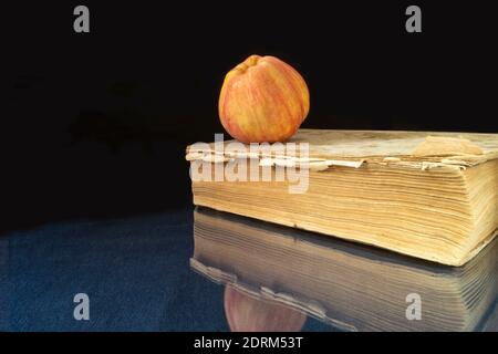 Das Buch und der Apfel ruhen auf einem Glastisch. Motive mit Reflexion auf schwarzem Hintergrund Stockfoto