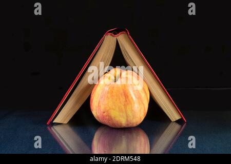 Das Buch und der Apfel ruhen auf einem Glastisch. Motive mit Reflexion auf schwarzem Hintergrund Stockfoto