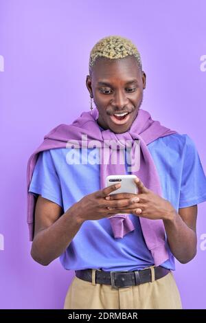 afrikanisches schwarzes männliches Modell mit Gerät, Smartphone verwenden, mit Freund chatten, Nachricht senden und Nachrichten teilen, isoliert auf violettem Hintergrund, ist er im Schock Stockfoto