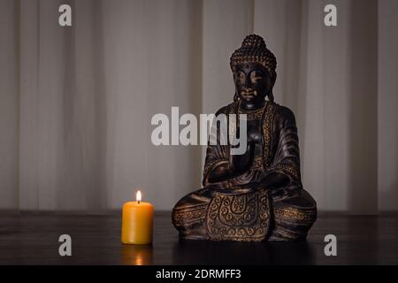 Buddha-Statue mit brennender Kerze auf Holztisch mit weichen strukturierten Hintergrund und dunkle Umgebung. Spiritualität, buddhismus und Religionskonzepte Stockfoto