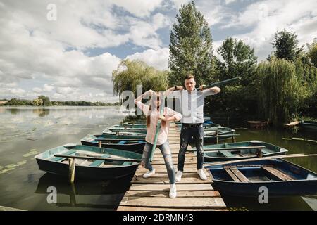 Junges Paar in der Liebe Spaß mit Rudern auf der Holzbrücke. Stilvolle Frau und Mann genießen Kanufahren auf sonnigen See Stockfoto