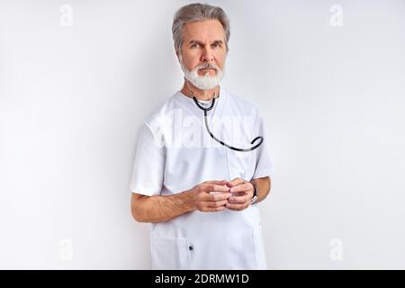Porträt von intelligenten reifen Arzt Mann mit grauen Haaren in medizinischen Uniform mit Stethoskop, posiert vor der Kamera, bereit zu helfen Stockfoto