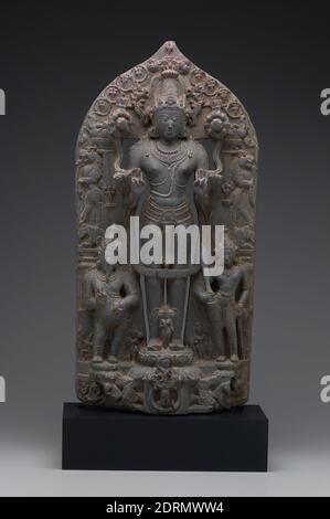 Sun God Surya with Adityas, Attendants, and Wives, late 11th Century, Schist, 74.9 × 35.6 × 14 cm (29 1/2 × 14 × 5 1/2 in.), Surya ist in beiden buddhistischen und hinduistischen Traditionen und ist eines der zwölf Adityas, oder Kinder der Göttin des Himmels. Identifiziert durch den Pferdewagen am Boden dieser Skulptur, hält er Lotos in seinen beiden Händen und ist umgeben von kleineren Darstellungen seiner elf Brüder. Pingala, die gebärtete und potbelierte Blockflöte, steht zu seiner Rechten, und Danda, die Messerin, steht zu seiner Linken und hält ein Schwert. Stockfoto