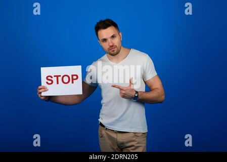 Schöner stilvoller Mann, der mit einem Schild in der Hand im Studio auf blauem Hintergrund steht. Stockfoto