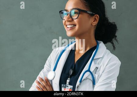 Porträt eines glücklichen schönen Arztes mit einem Stethoskop an einer Wand. Junge medizinische Fachkraft trägt eine Uniform und lächelt drinnen. Stockfoto