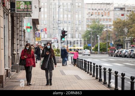 BELGRAD, SERBIEN - 17. OKTOBER 2020: Zwei junge Frauen mit einer Atemmaske, die Apps auf ihren Smartphones in der Straße von Belgrad überprüfen, Dur Stockfoto